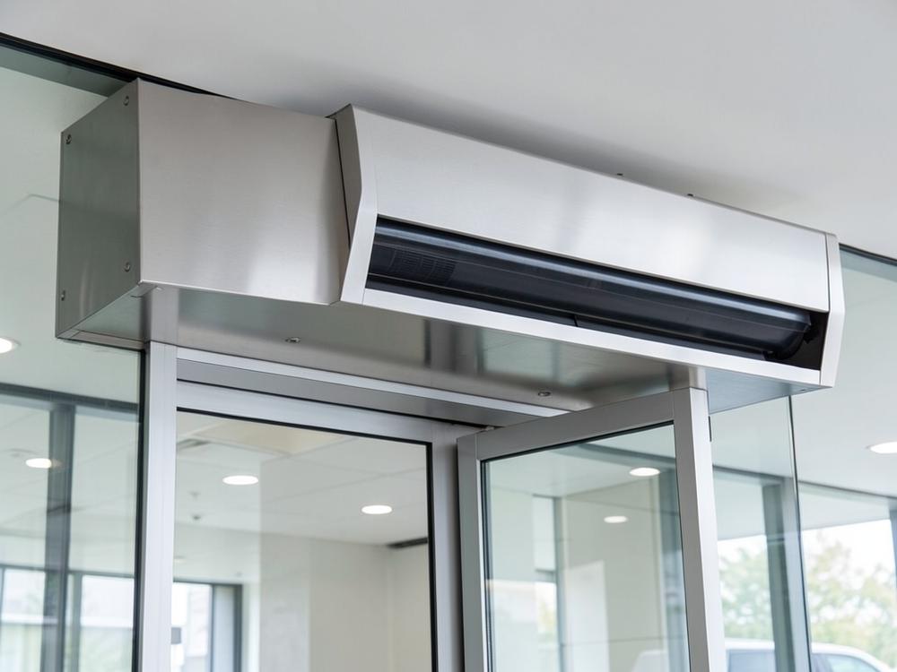 Stainless steel air curtain unit mounted above a glass entrance door